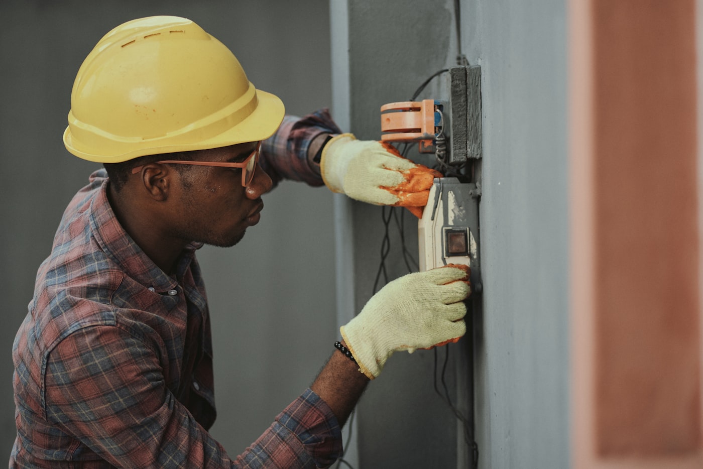 Electrician in a hard hat working on a wall-mounted electrical box